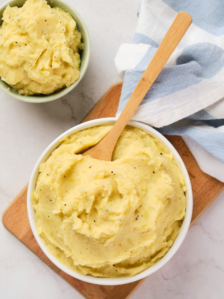 A bowl of garlic mashed potatoes with a wooden spoon on top.