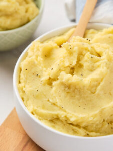 A bowl of creamy garlic mashed potatoes with a wooden spoon.