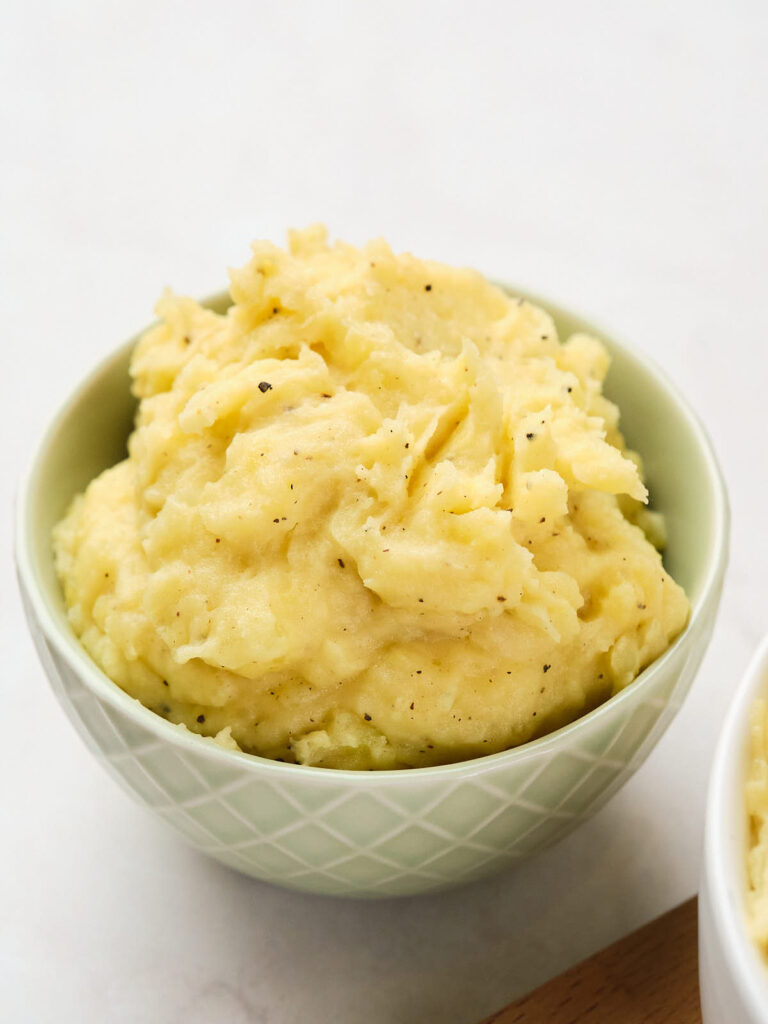 A bowl of garlic mashed potatoes seasoned with black pepper is placed on a white surface.