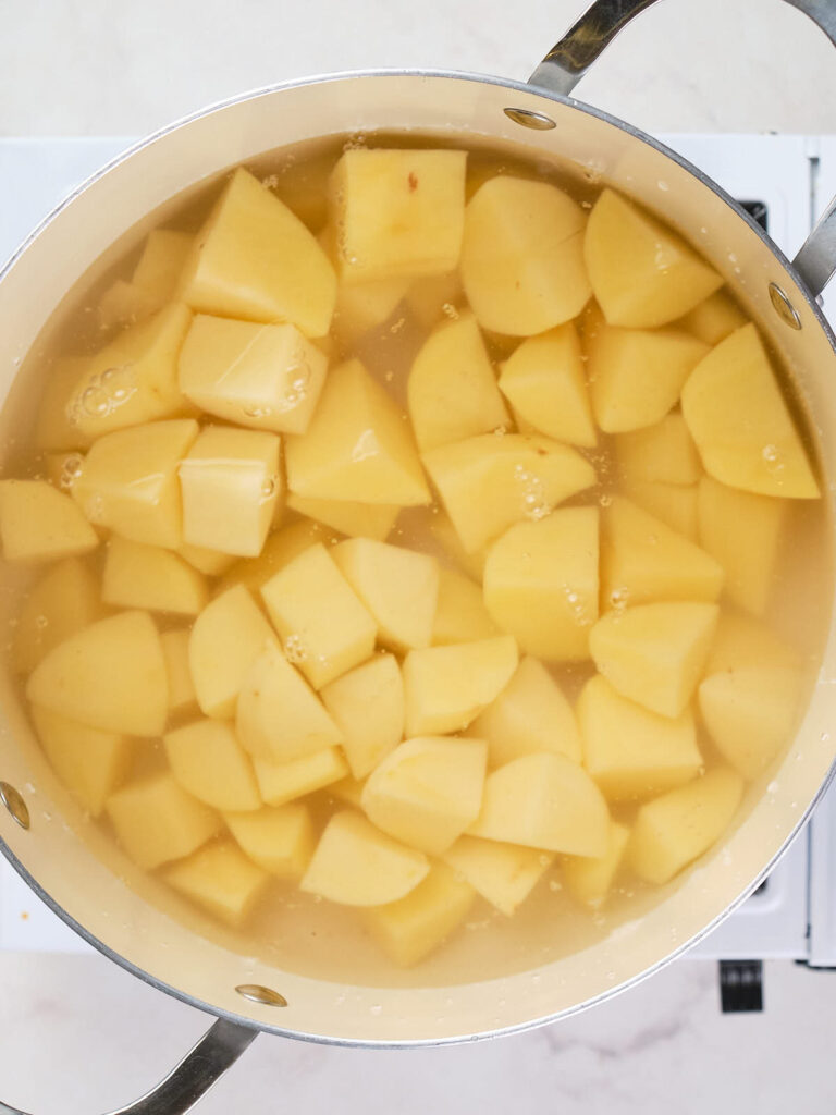 A pot filled with cubed potatoes submerged in water, ready for boiling.