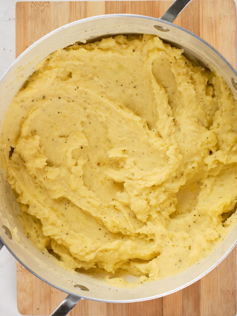 A pot of creamy mashed potatoes on a wooden surface.