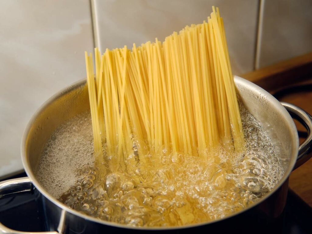 Uncooked spaghetti being added to a pot of boiling water on a stovetop.