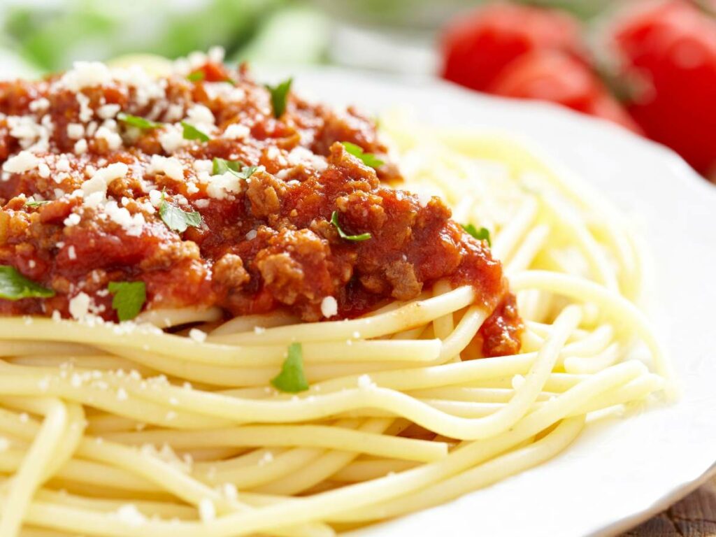 A close-up of a plate of spaghetti topped with tomato-based meat sauce, garnished with grated cheese and parsley.