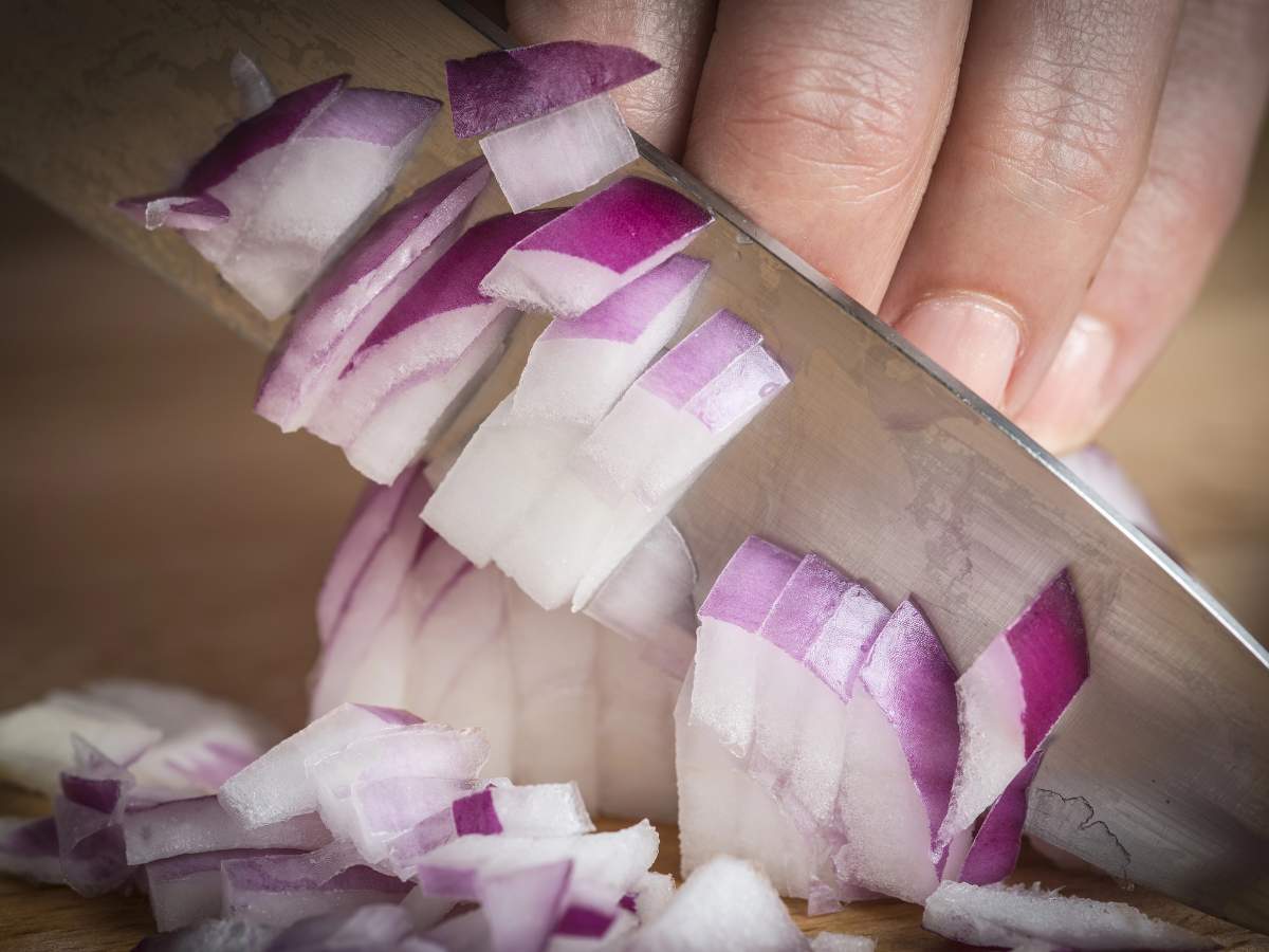 A hand is slicing a purple onion on a cutting board.