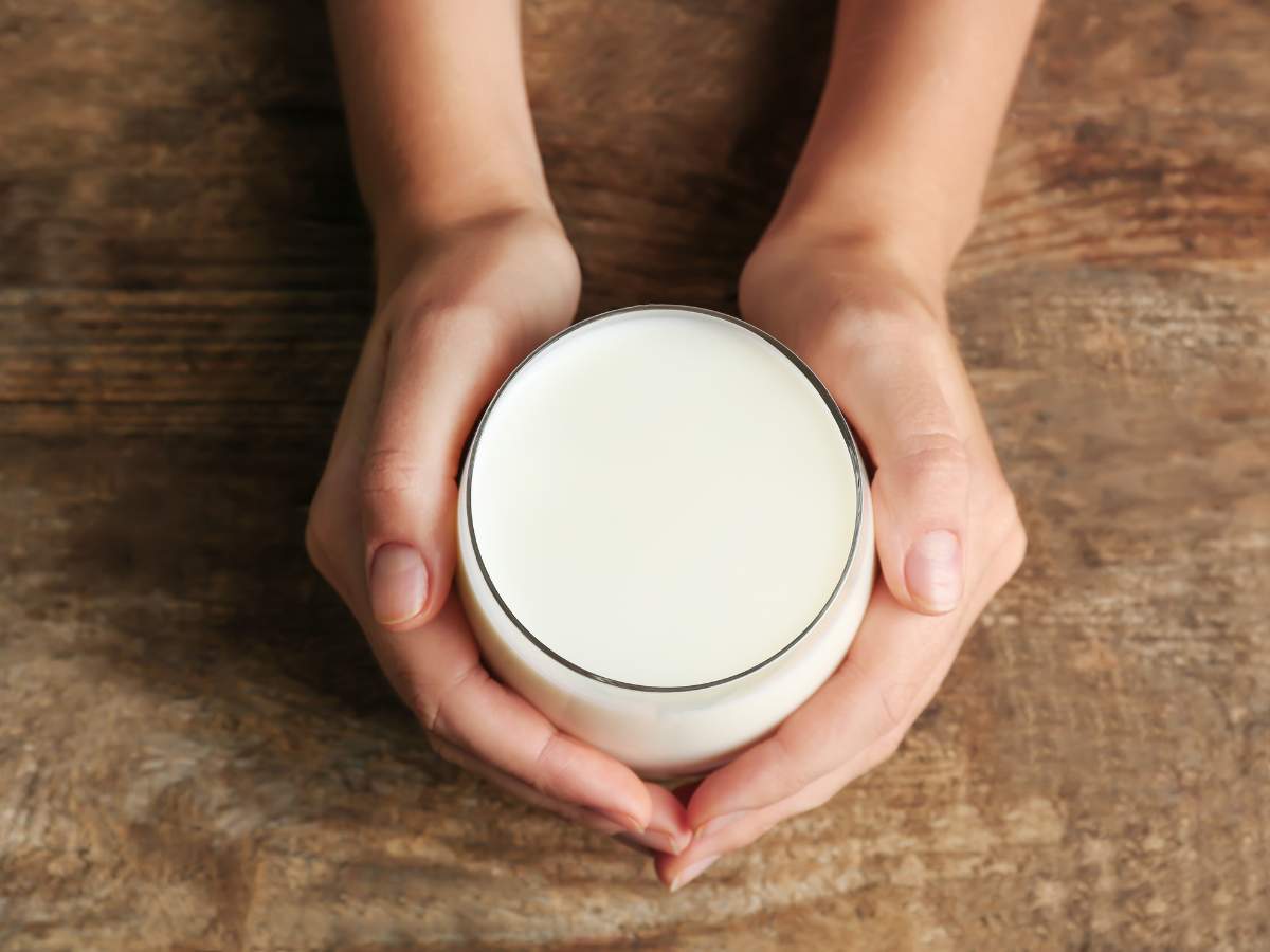 A pair of hands holding a glass of milk over a wooden table.