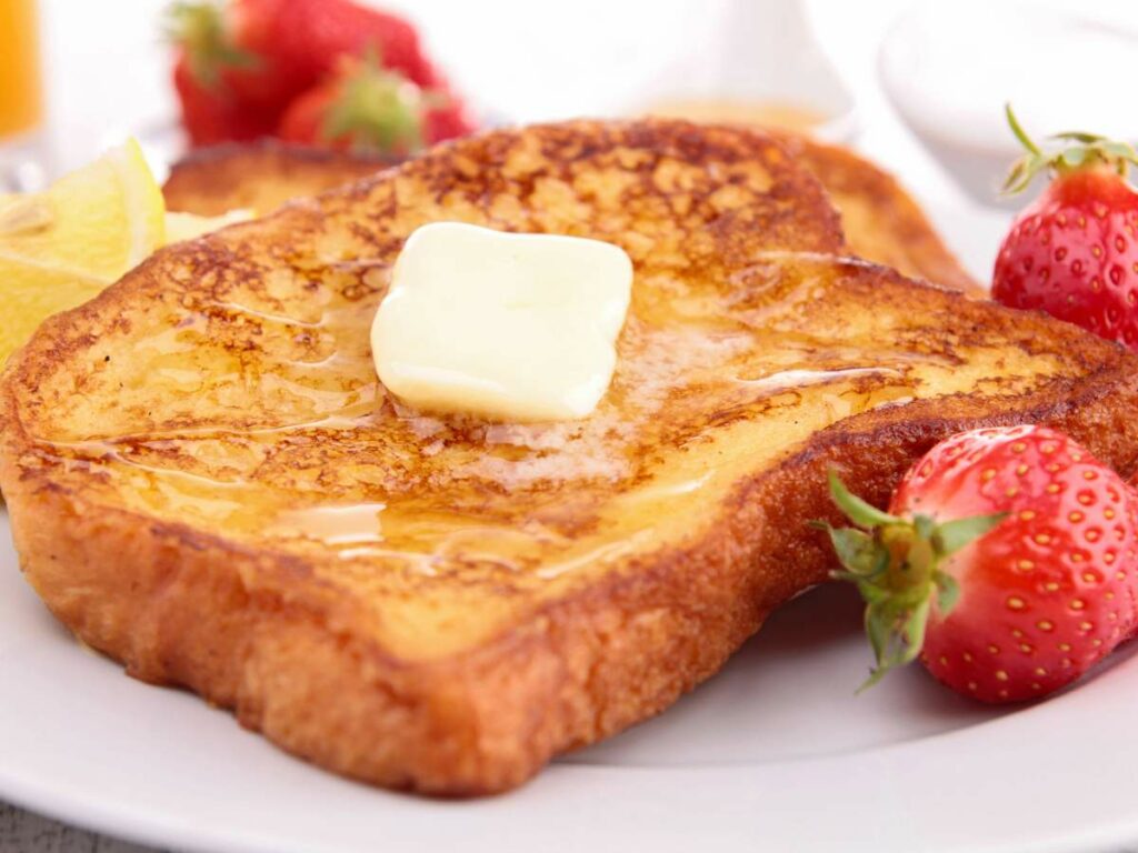 A plate with two pieces of French toast topped with a pat of butter and syrup, accompanied by fresh strawberries.