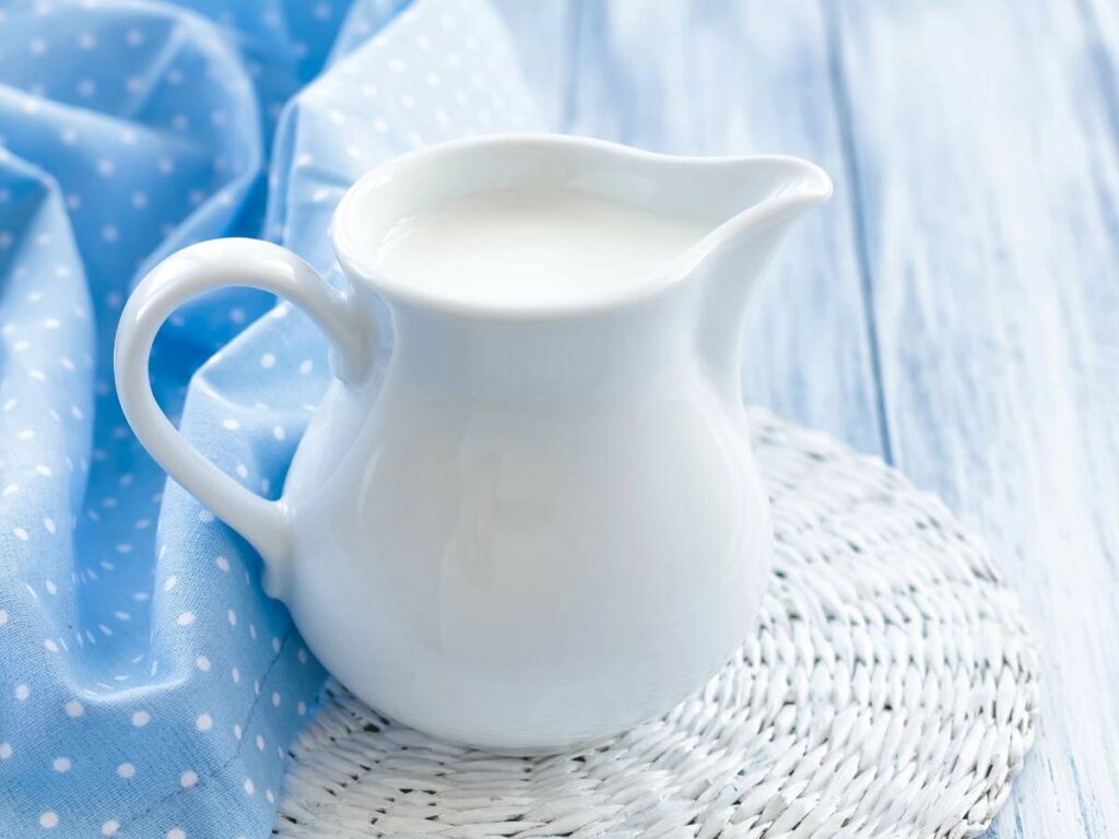 A white ceramic pitcher filled with milk is placed on a woven mat.