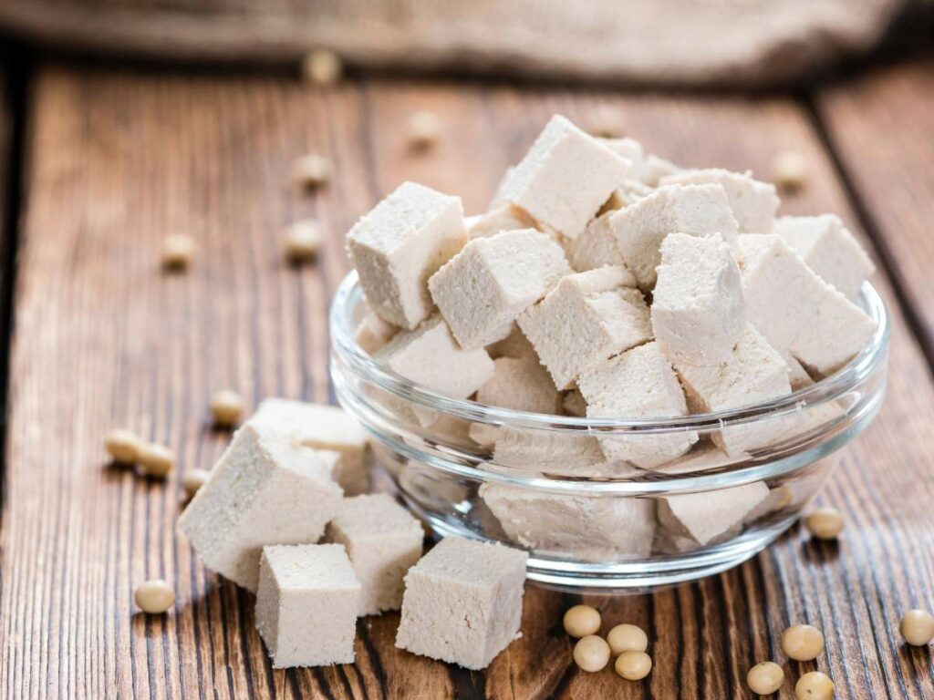 A clear glass bowl filled with cubed tofu, placed on a wooden surface.