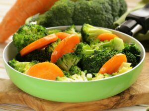 A bowl of steamed broccoli and carrot slices on a wooden table.