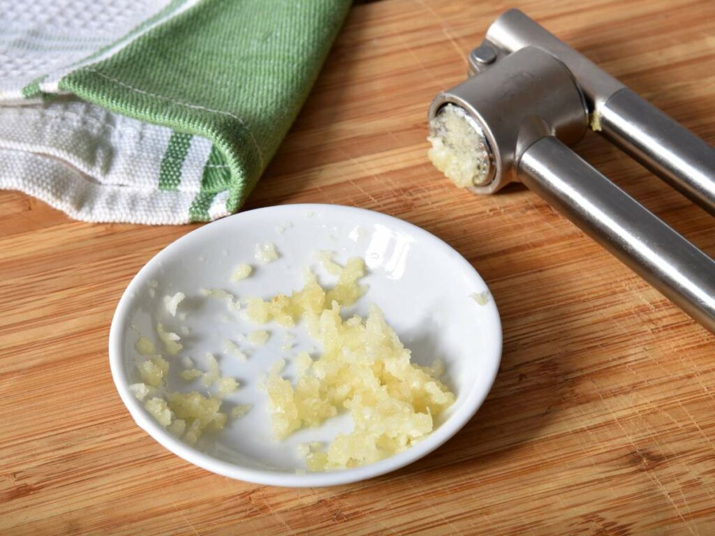 A small white dish with minced garlic sits on a wooden surface.