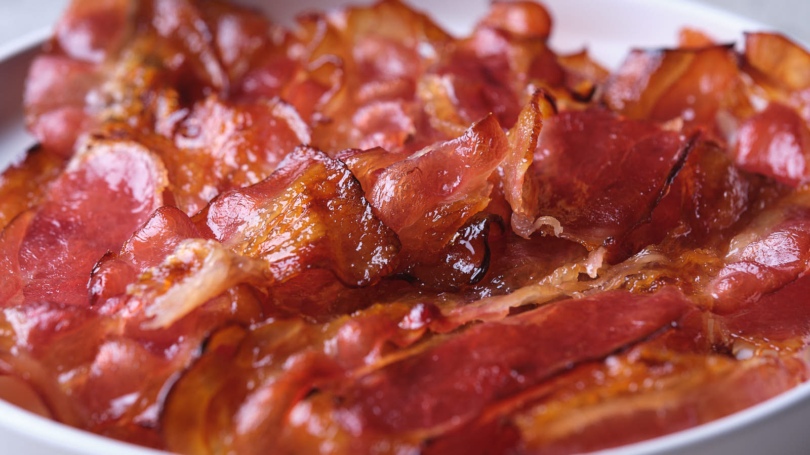 Close-up of crispy, cooked maple bacon slices in a white dish.