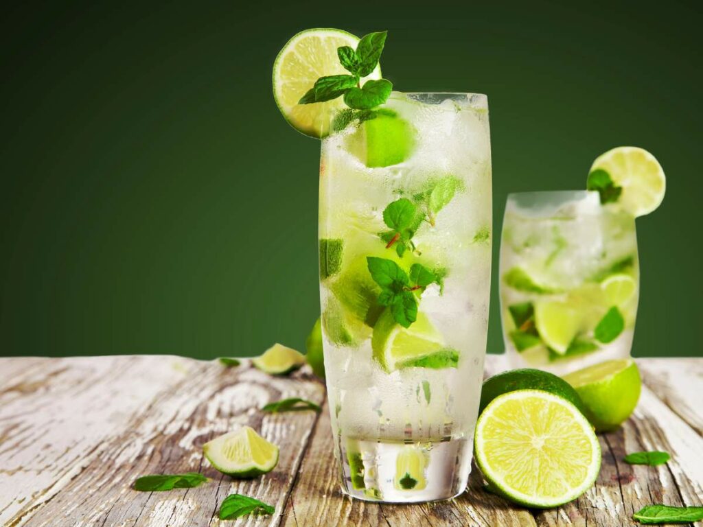 Two tall glasses of a lime and mint cocktail with ice, garnished with lime.