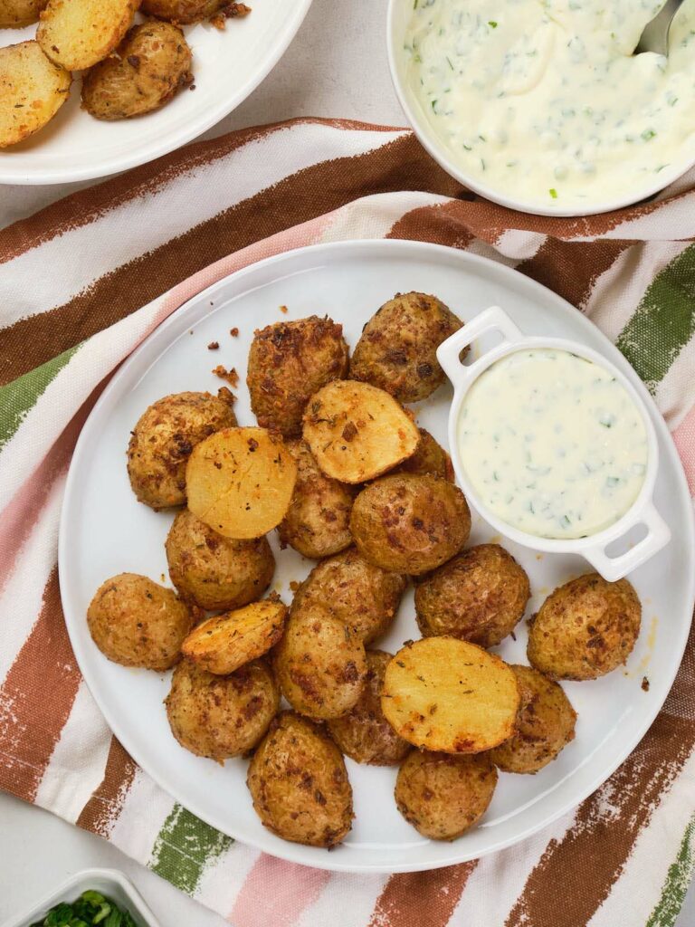 A white plate with parmesan potatoes and a small bowl of creamy dipping sauce.