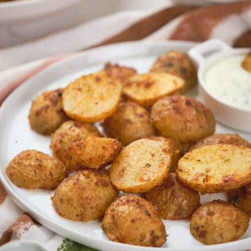 A plate of parmesan potatoes with a small dish of creamy dipping sauce next to them.