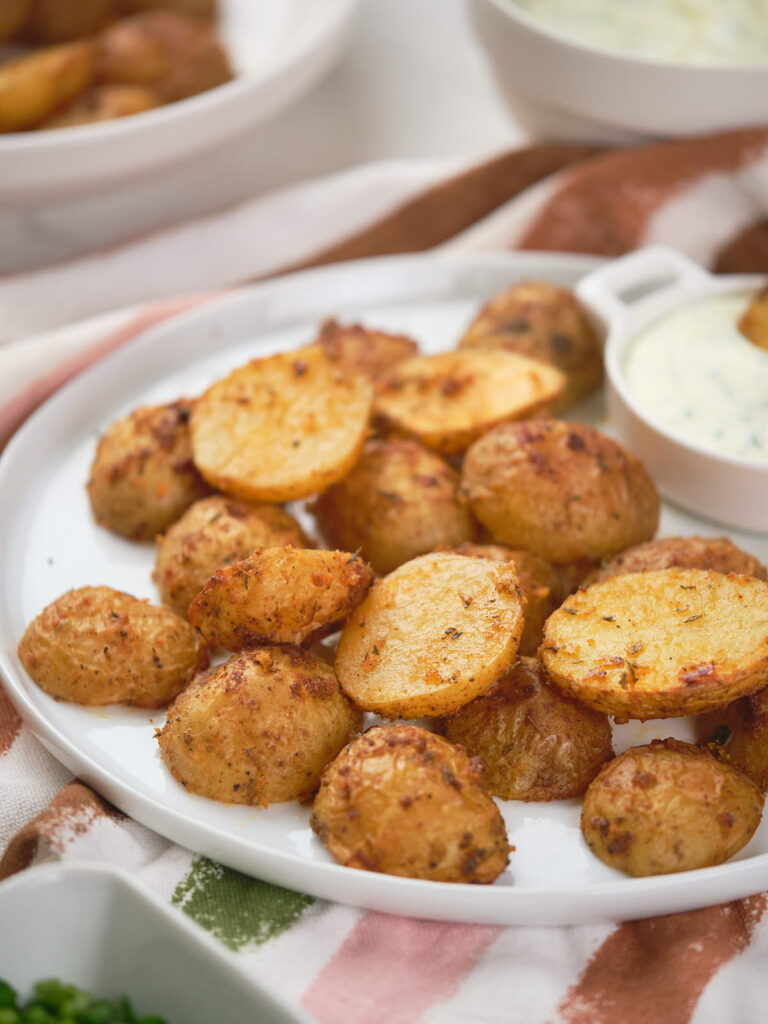 A plate of parmesan potatoes with a small dish of creamy dipping sauce next to them.