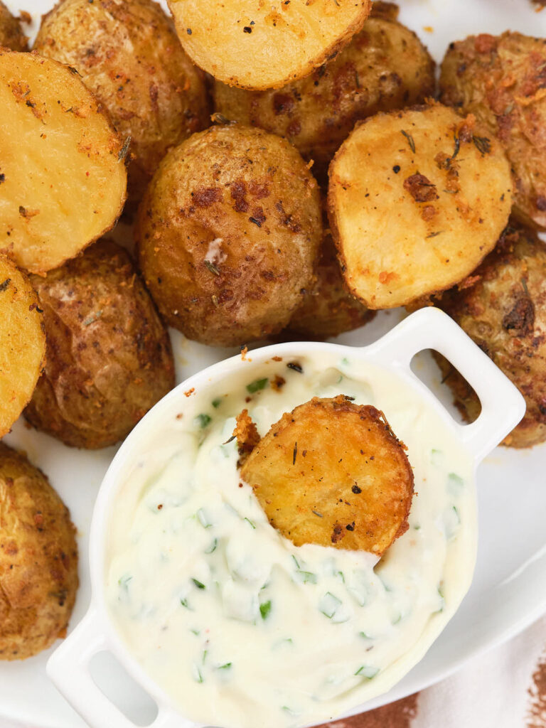 A plate of parmesan potatoes with one partially dipped in a small white bowl of creamy herb dip.