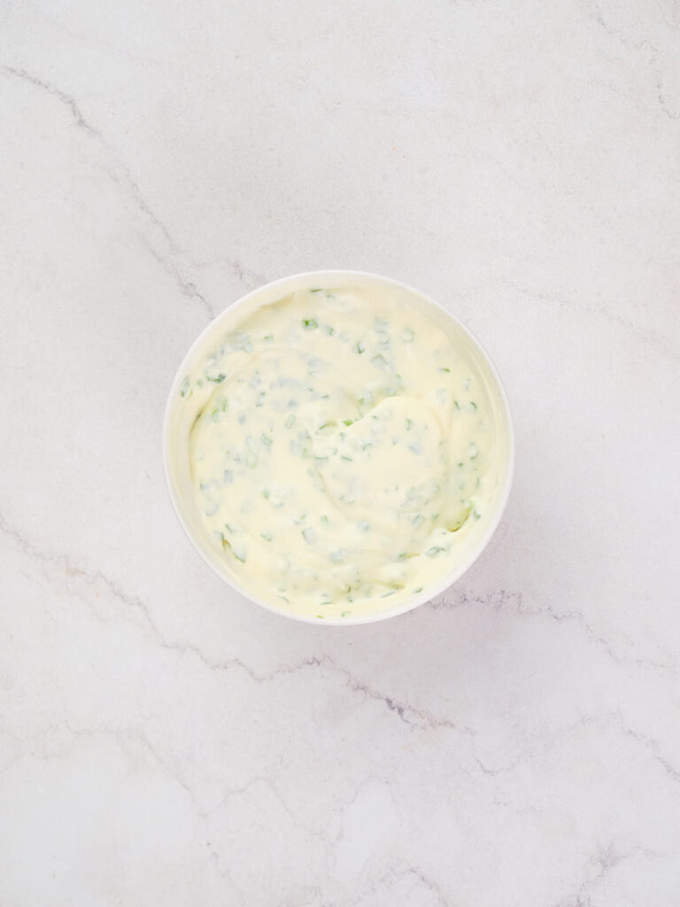 A white bowl filled with a creamy, pale yellow sauce with green herb specks.