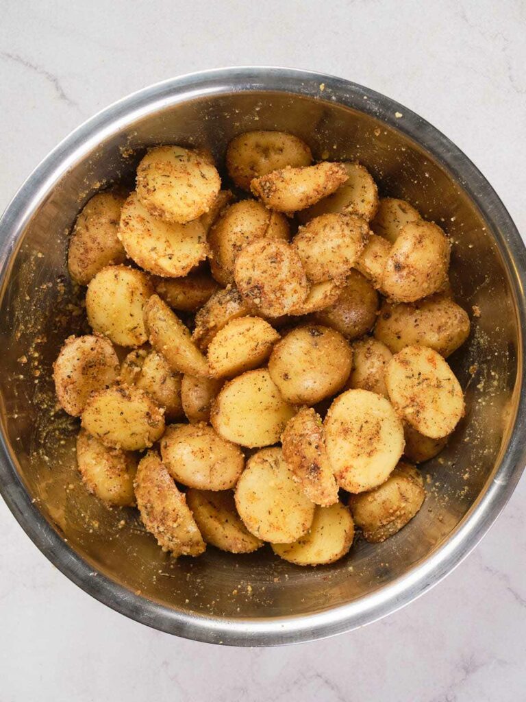 A stainless steel bowl filled with seasoned and halved roasted potatoes.