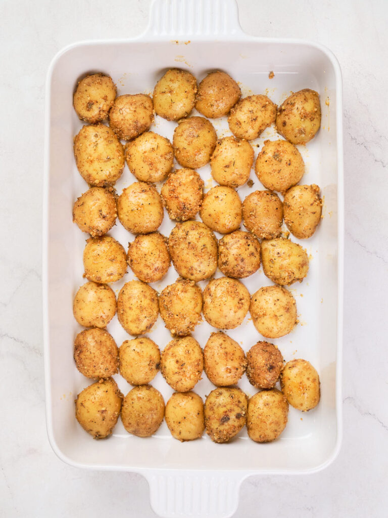 A white rectangular dish filled with evenly spaced, round, seasoned roasted potatoes.