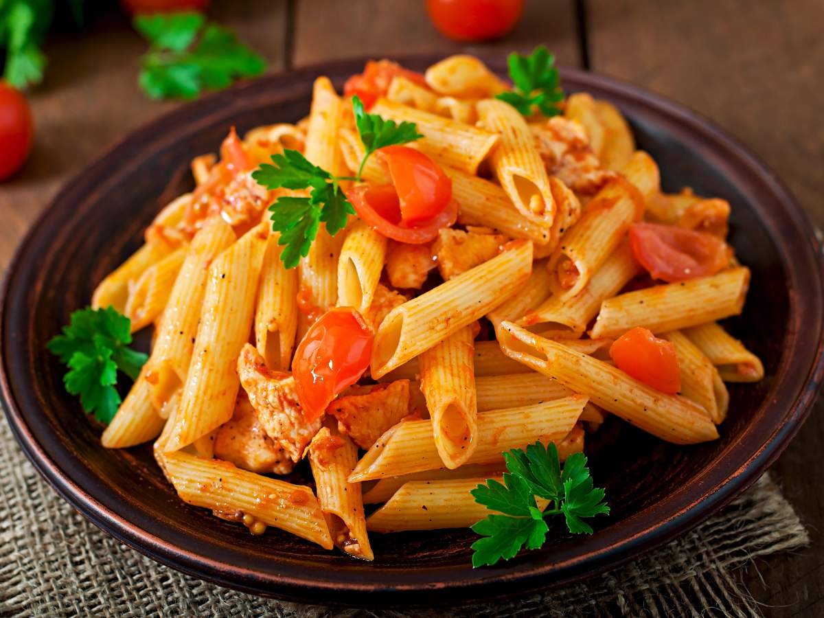 A plate of penne pasta mixed with chunks of chicken, tomatoes, and garnished with fresh parsley.