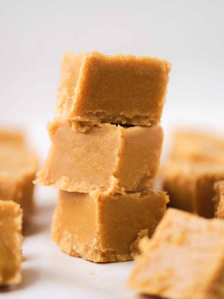 A stack of three pieces of peanut butter fudge with more pieces blurred in the background.