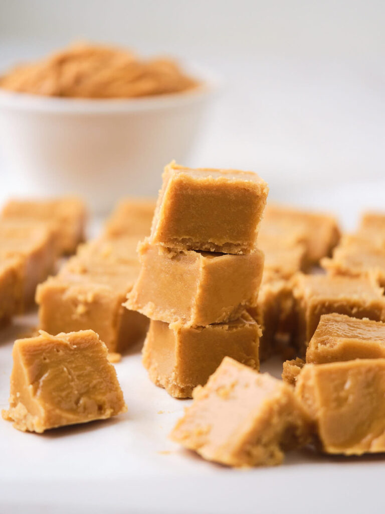 A pile of peanut butter fudge cubes is stacked in the foreground with more pieces scattered around.