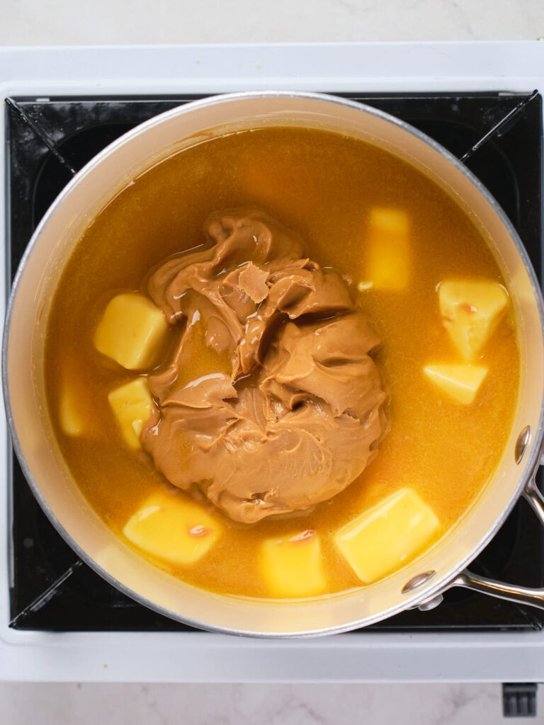 A pot on a stove containing a mixture of melted butter and peanut butter, partially blended together.