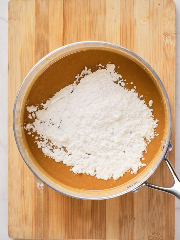 A mixing bowl containing a brown batter with a large amount of white dry ingredient on top.