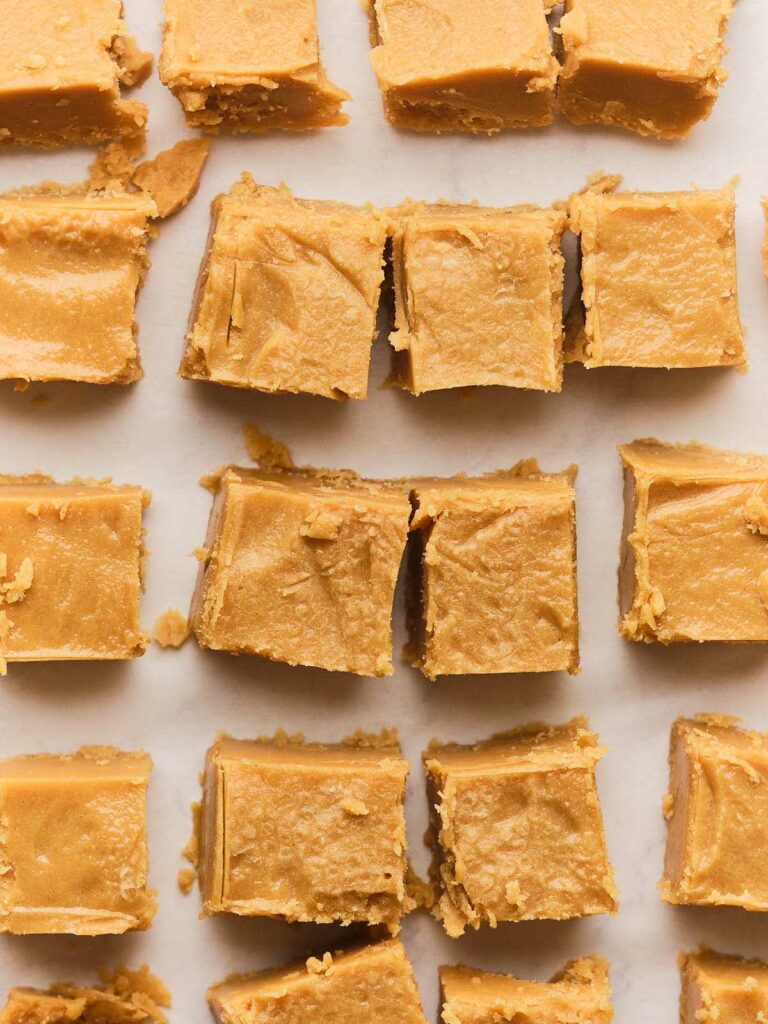 Close-up of multiple squares of peanut butter fudge arranged in rows on a light surface.