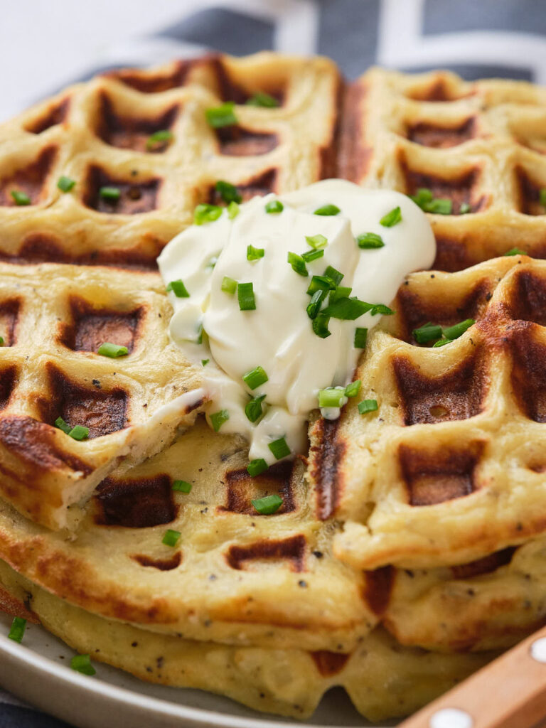 A close-up of potato waffles topped with a dollop of cream and garnished on a plate.