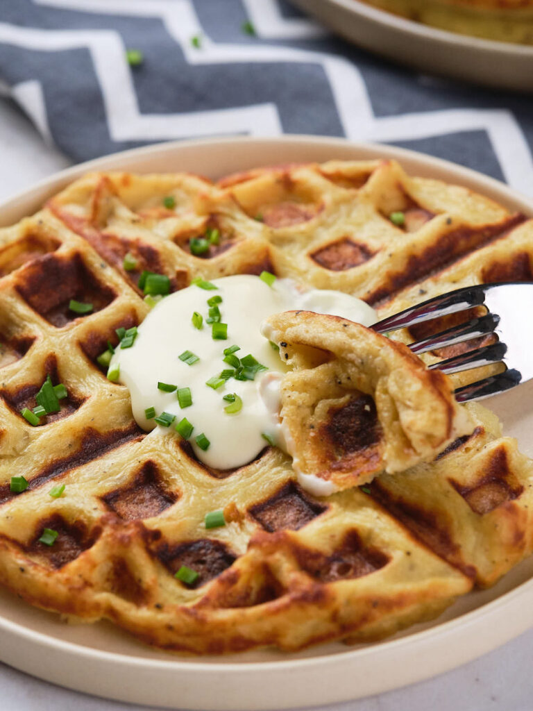 A plate of potato waffles with a fork picking up a bite-sized piece.