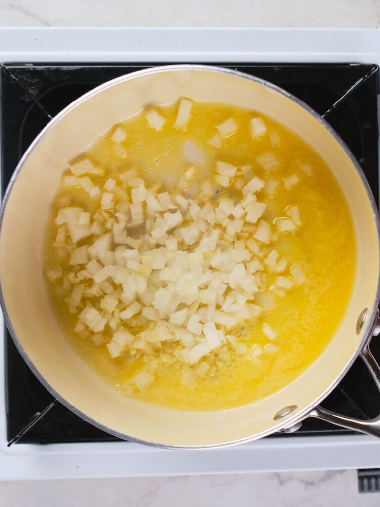 A pot of diced onions being sautéed in melted butter on a stovetop.