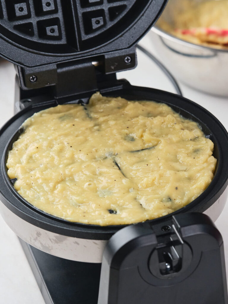 A waffle maker filled with a raw mixture of batter, ready to be cooked.