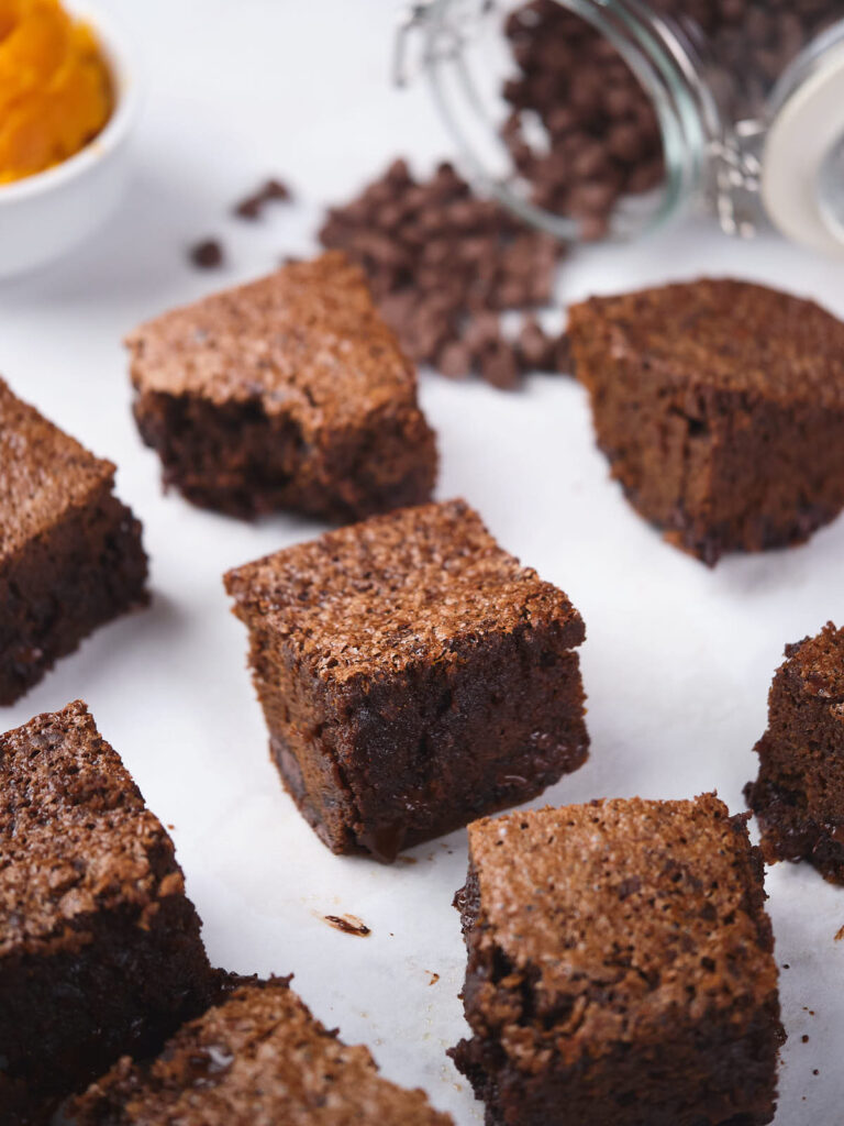 Several pieces of pumpkin brownies are arranged on a white surface.