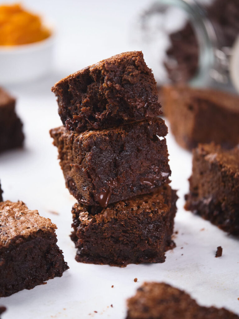 A stack of three pumpkin brownies with a few more brownies scattered around on a white surface.