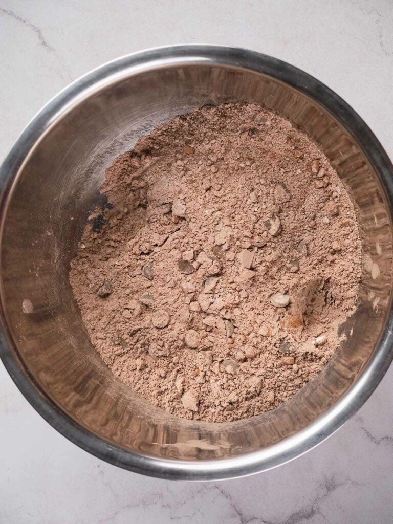 A metal bowl containing dry ingredients for brownies on a marble countertop.