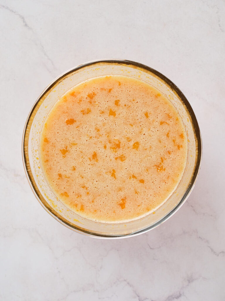 A bowl containing a light orange mixture on a white marble surface.