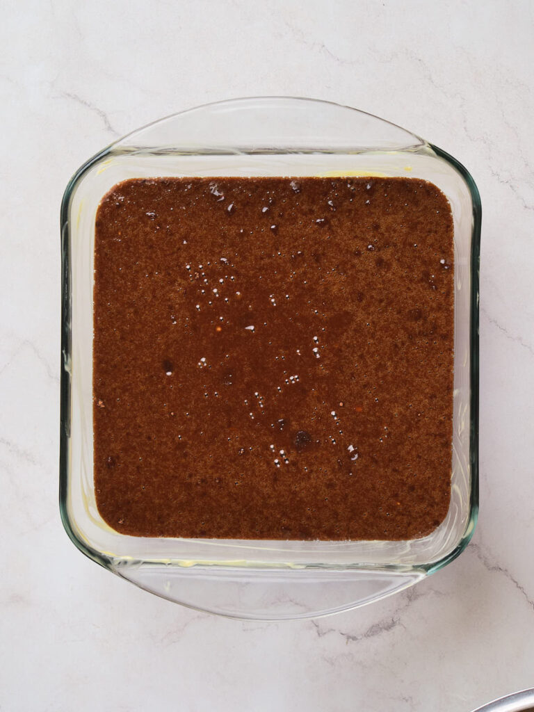 A glass baking dish filled with raw brownie batter on a light-colored marble surface.