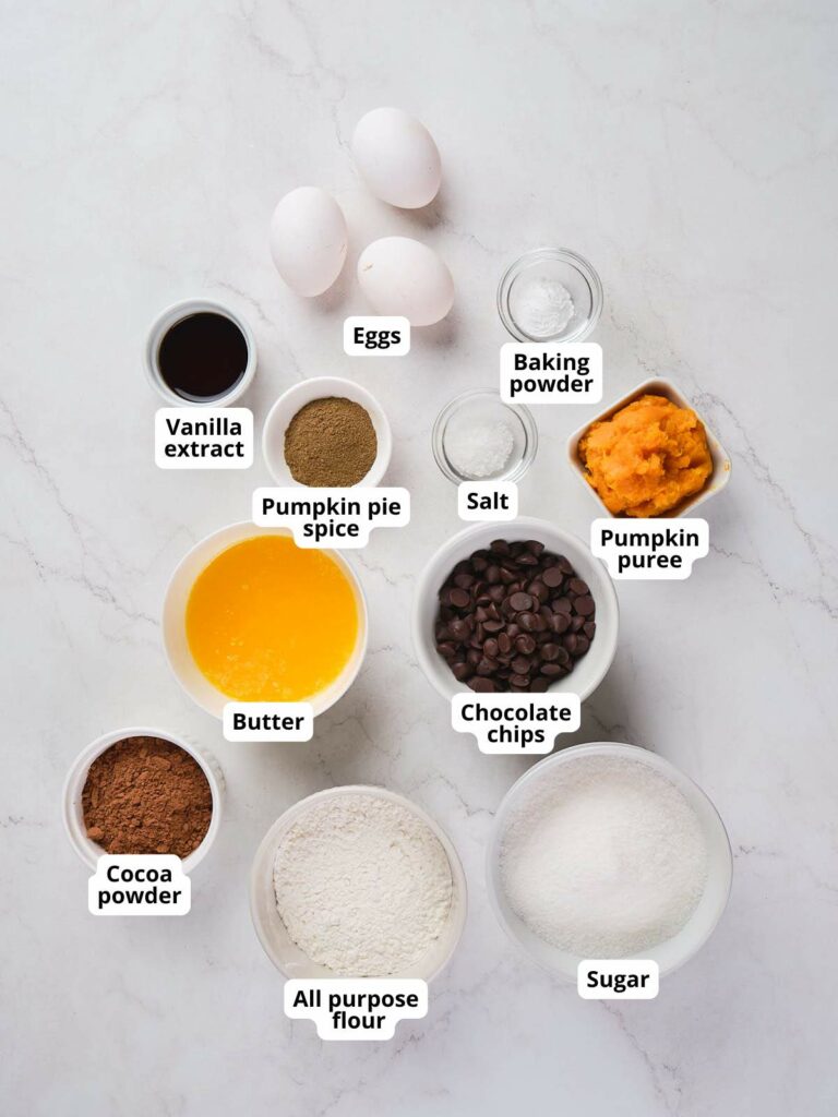 Ingredients for pumpkin brownies are arranged on a white surface.