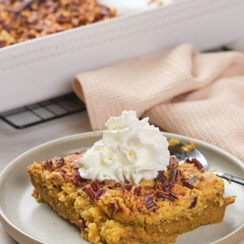 A slice of pecan-topped pumpkin dump cake with a dollop of whipped cream on a plate.