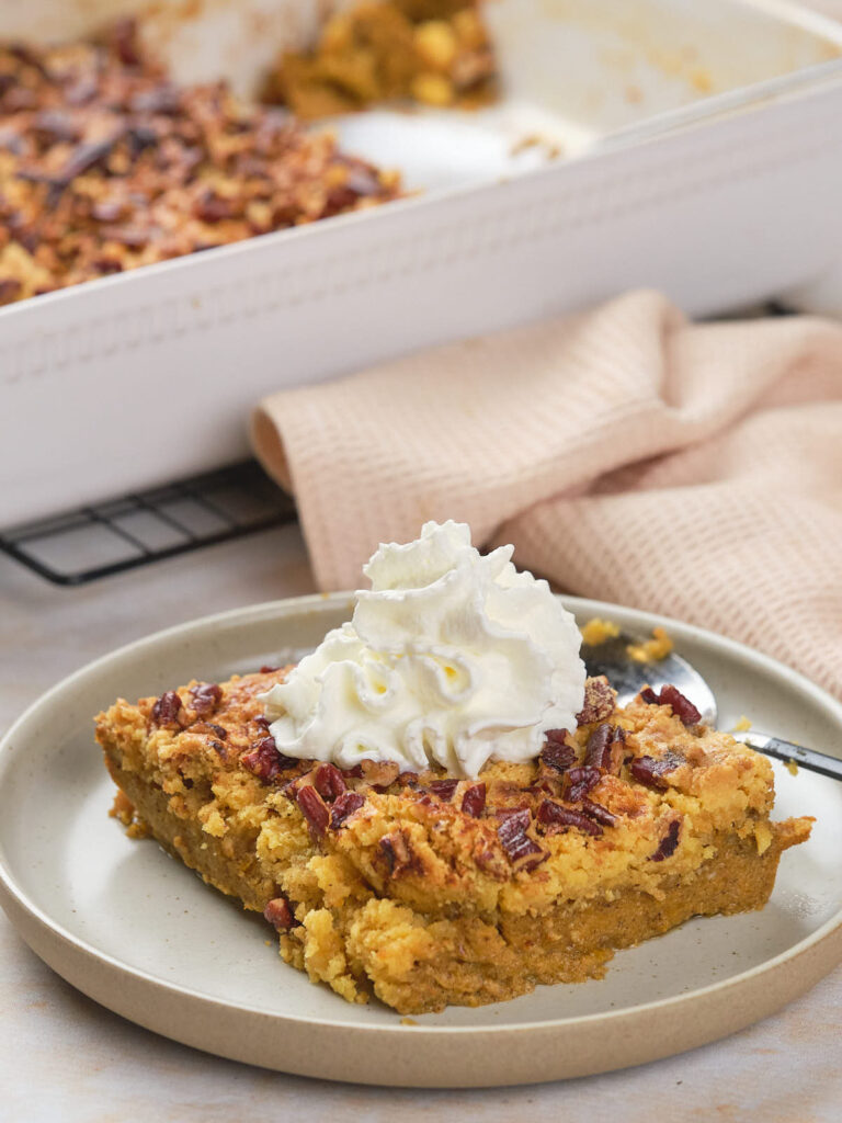 A slice of pecan-topped pumpkin dump cake with a dollop of whipped cream on a plate.