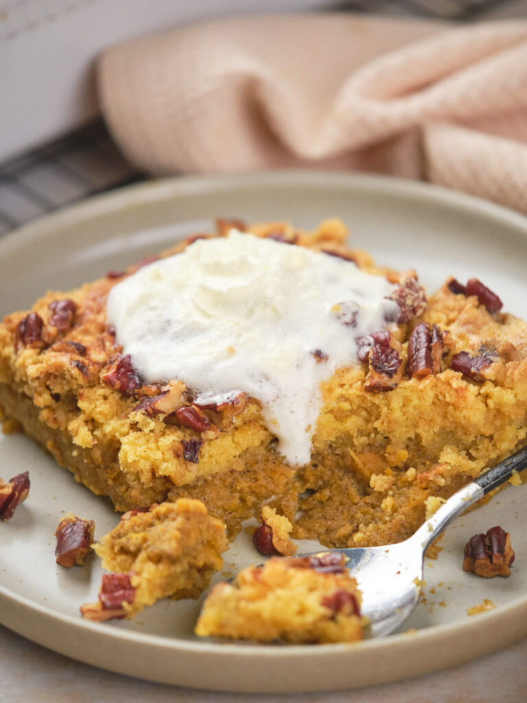 A piece of pumpkin dump cake topped with whipped cream and pecans on a plate with a spoon.