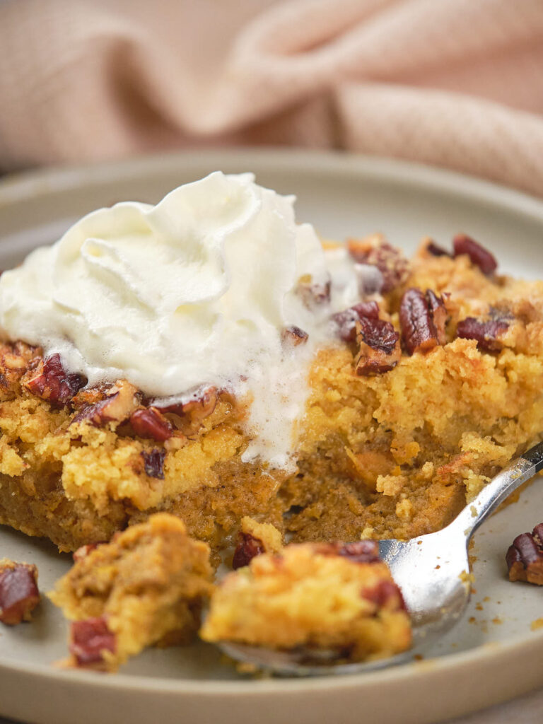 A close-up of pumpkin dump cake, topped with pecans and a dollop of whipped cream.