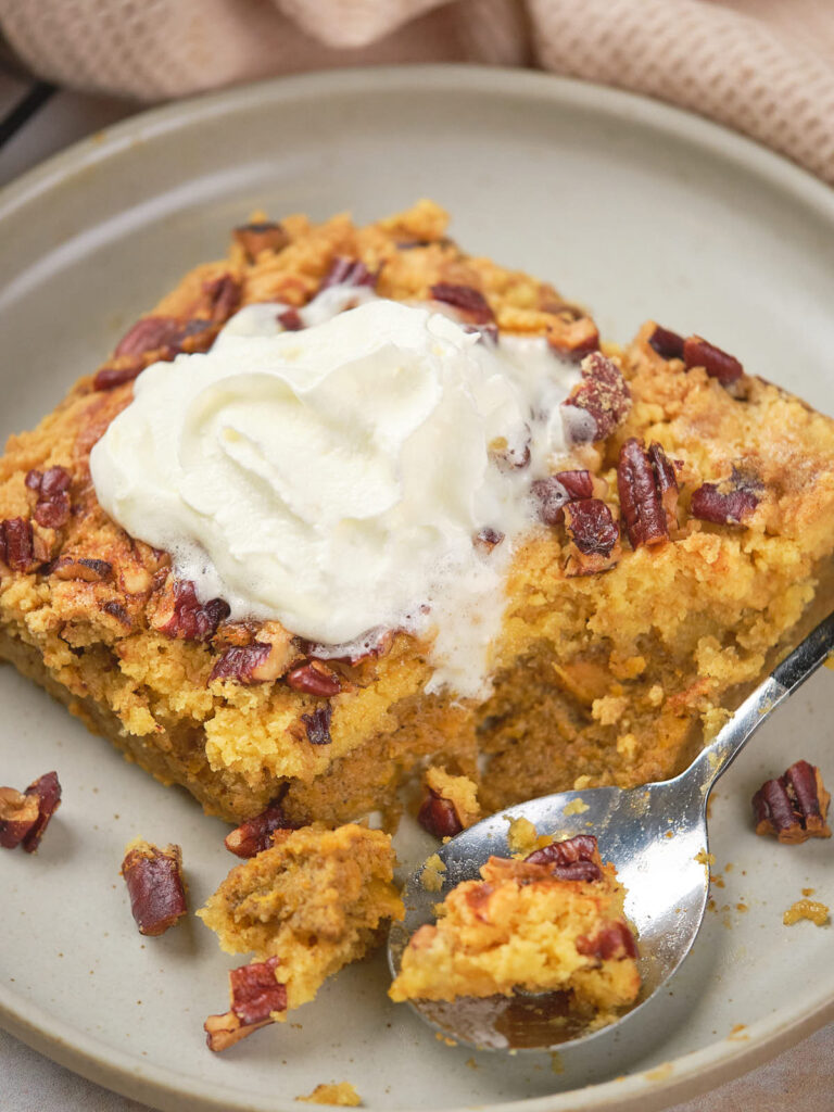 A piece of pumpkin cake topped with whipped cream and chopped nuts on a plate.