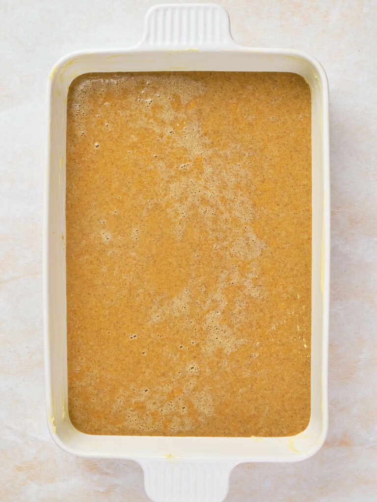 Rectangular white baking dish filled with a light brown batter, seen from above, ready to be baked.