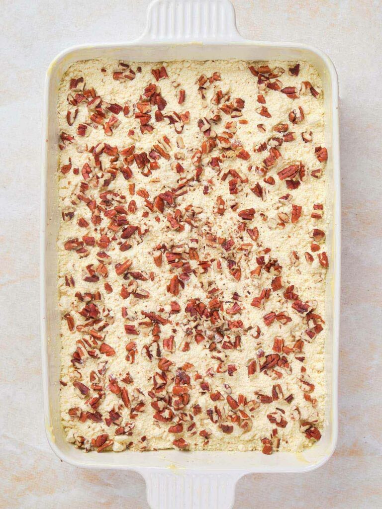 A rectangular baking dish filled with a cream-colored mixture topped with chopped pecans.