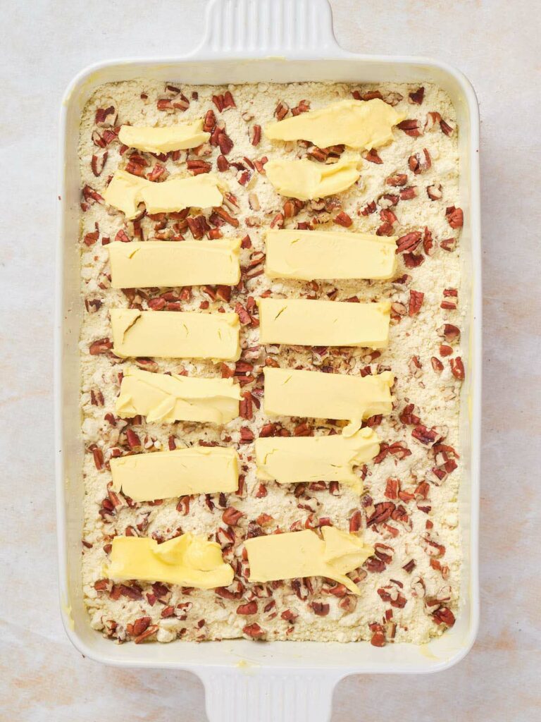 A casserole dish filled with dry cake mix, chopped nuts, and topped with evenly spaced slices of butter.