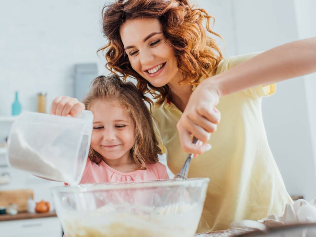 A woman and a girl smile as they bake together.