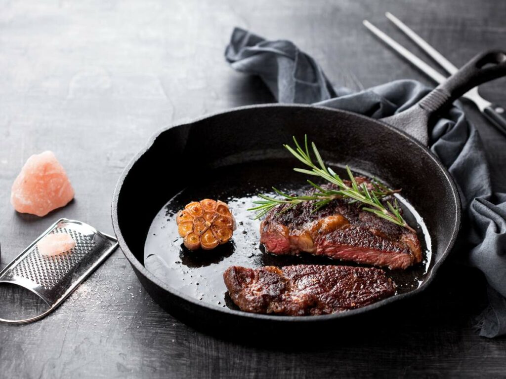 A cast-iron skillet with cooked steak, garnished with a sprig of rosemary.