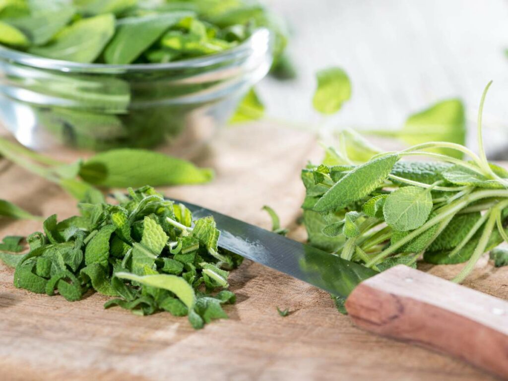 A knife with a wooden handle cutting fresh green herbs on a wooden surface.